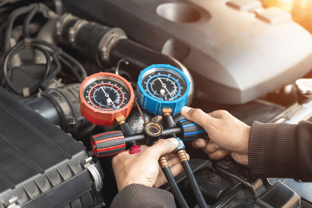 car a/c issues, auto repair in Hanover, PA at Alex's Autoworks. Technician using A/C manifold gauge set with red and blue pressure dials to check a car’s air conditioning system under the hood.