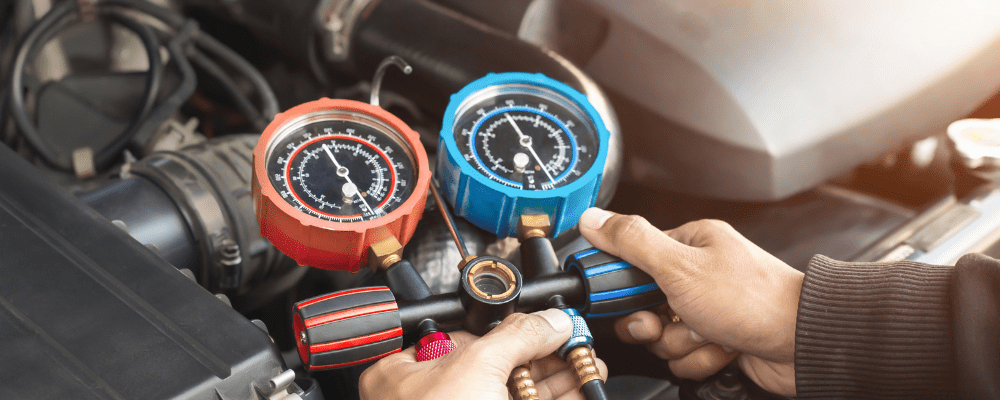 car a/c issues, auto repair in Hanover, PA at Alex's Autoworks. Technician using A/C manifold gauge set with red and blue pressure dials to check a car’s air conditioning system under the hood.