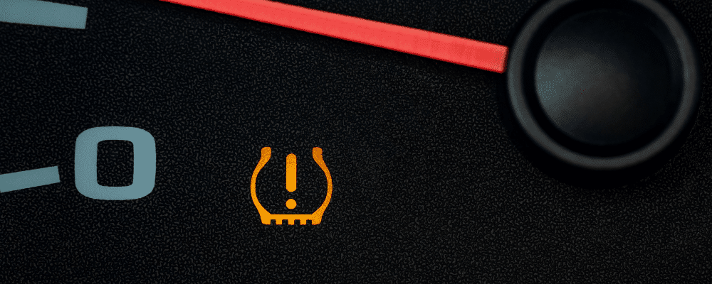 TPMS service, auto repair in Hanover, MA by Alex’s Autoworks. Image of a dashboard warning light indicating low tire pressure, highlighting the importance of proper tire maintenance for safety and performance.